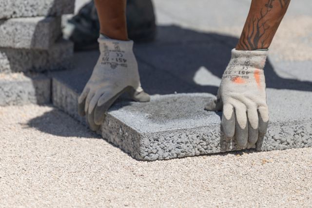 Mains positionnant un pavé sur le lit de pose